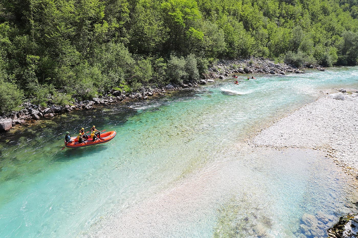 A group on a raft and kayakers descend the Soča river rapids