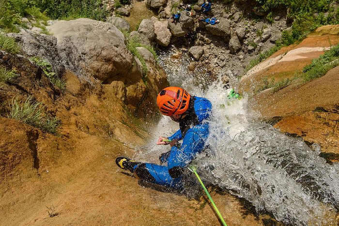 Canyoneer steigt mit einem Seil den Wasserfall hinunter, wo eine Gruppe auf ihn wartet