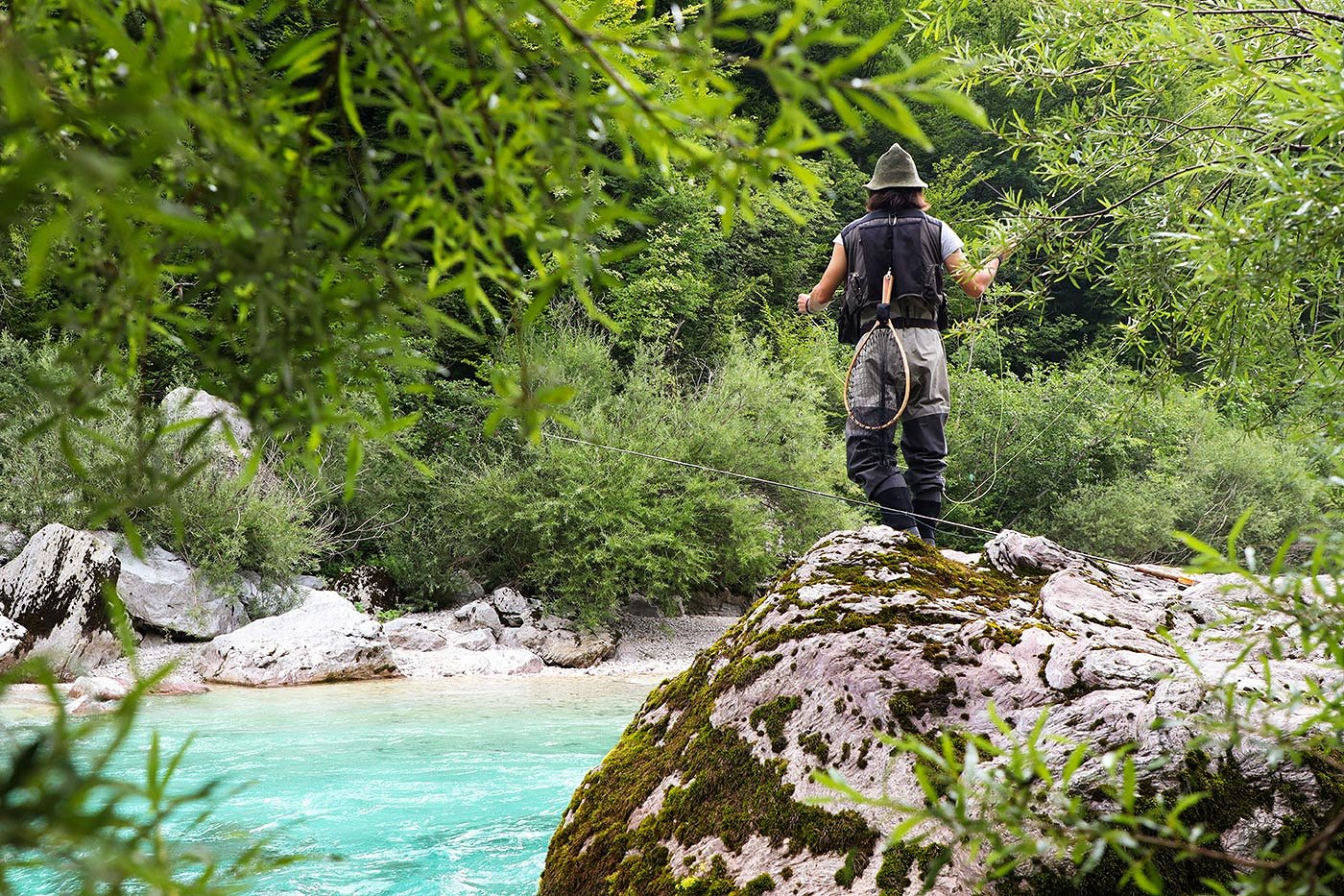 Un pescatore a mosca su una roccia vicino al fiume Isonzo color smeraldo
