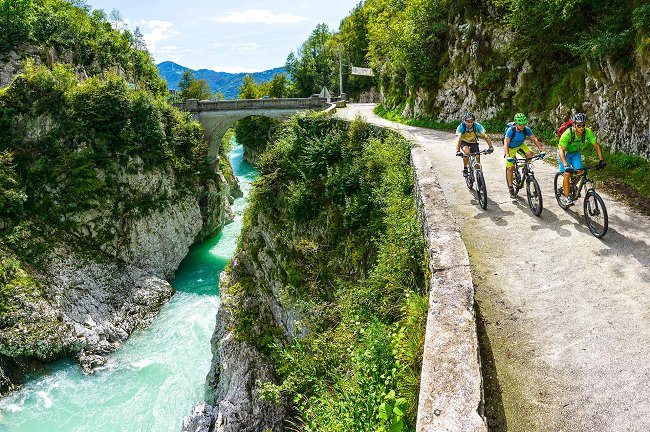 Tre ciclisti in sella oltre il ponte Napoleone vicino a Kobarid