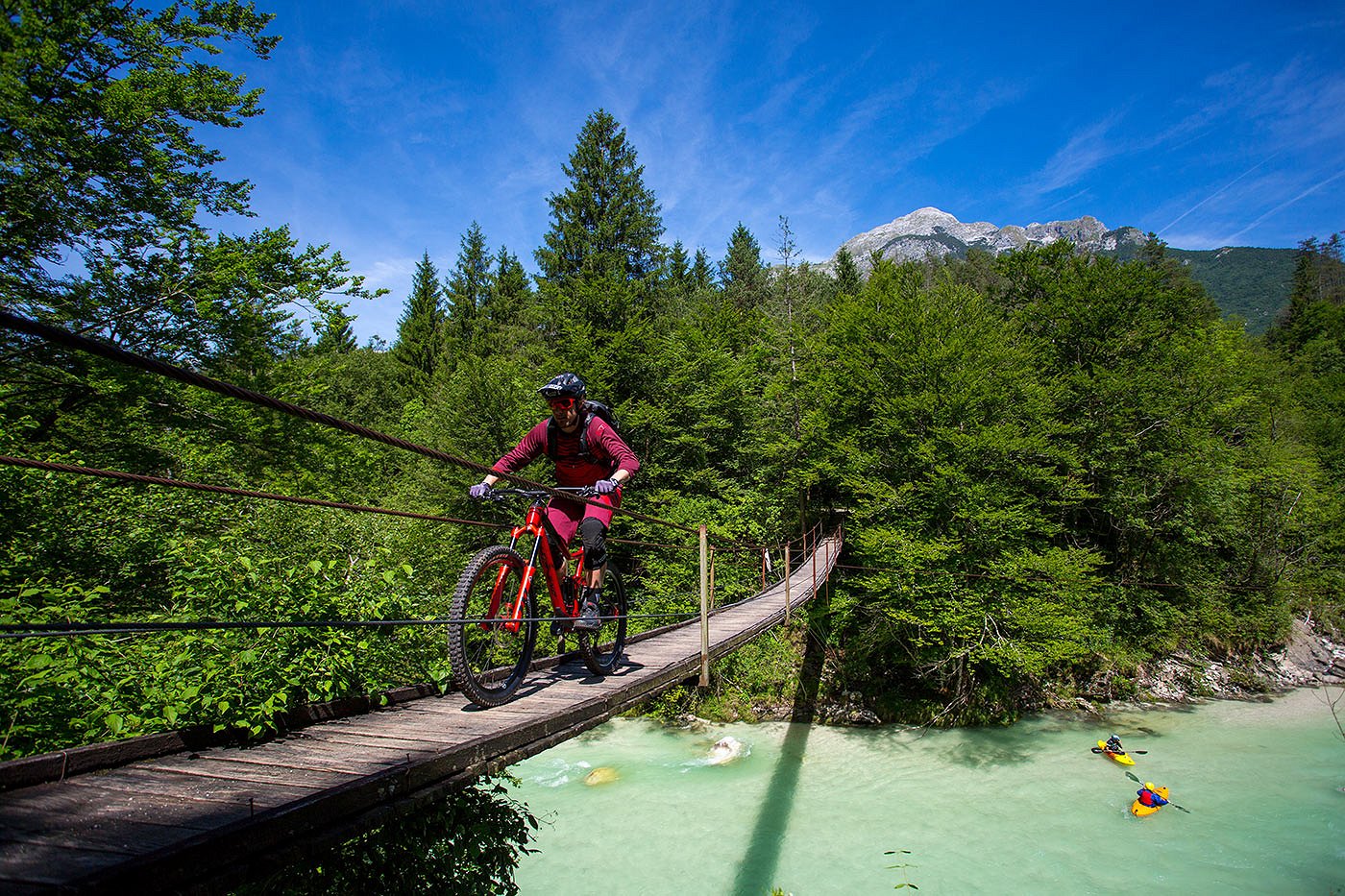 Ein Radfahrer überquert die Hängebrücke über den Fluss Soča, auf dem der Kajakfahrer absteigt