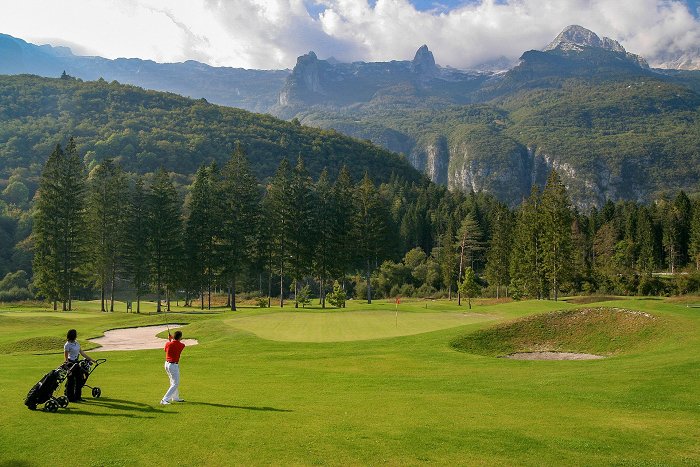 The couple is playing golf on a green surrounded by hills