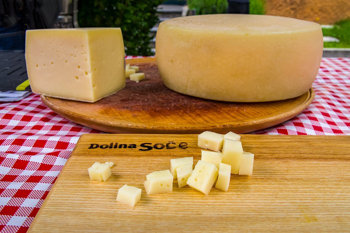 Na kocke narezan sir na deski, v ozadju celo kolo sira
