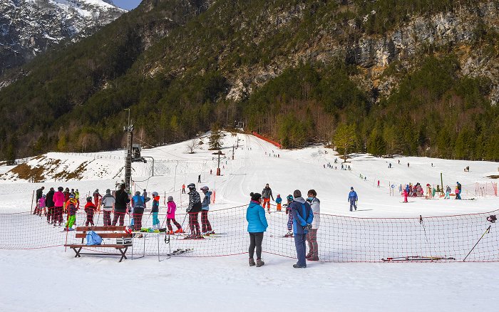 Ein schneebedecktes Skigebiet mit zwei Skiliften, das von Kindern jeden Alters genutzt wird.