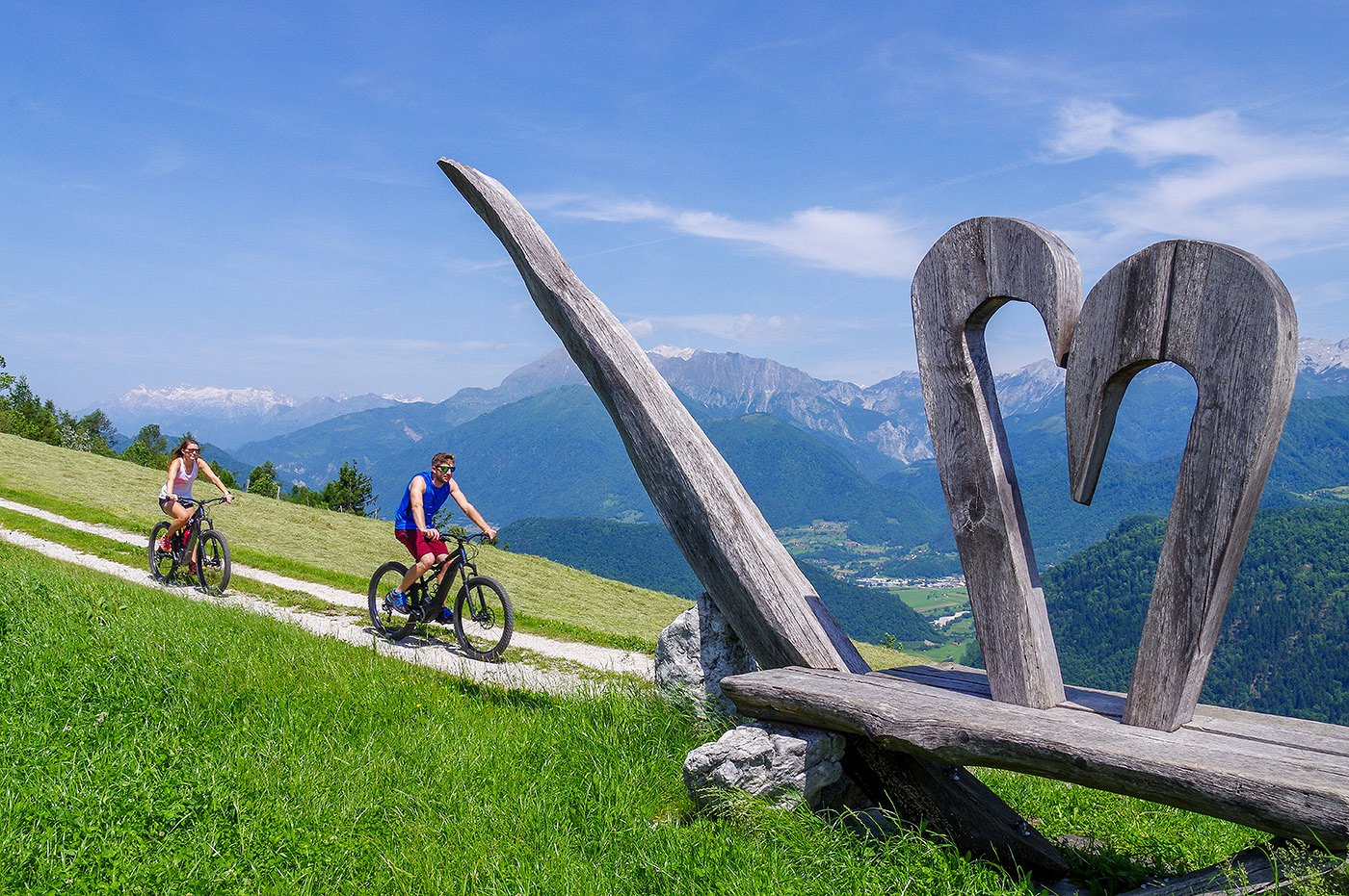 Kolesarja kolesarita mimo skulpture na Širokem z razgledom na dolino