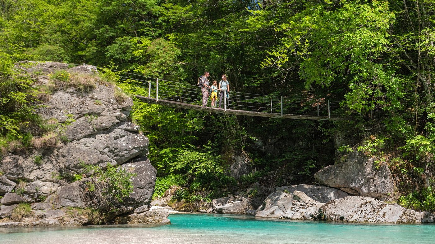 The family of hikers enjoys nature on the footbridge under which the emerald river Soča flows