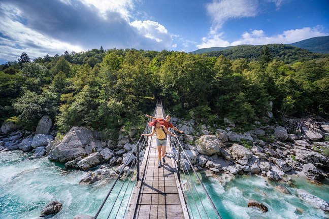 Hikers walk on a wooden hanging bridge over the rapids of the Soča River.