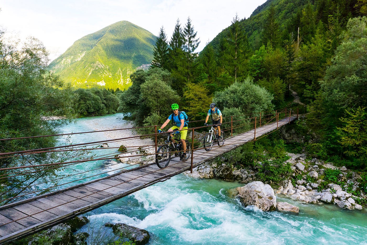 Mountain bikers cross the Soča River on a wooden hanging bridge