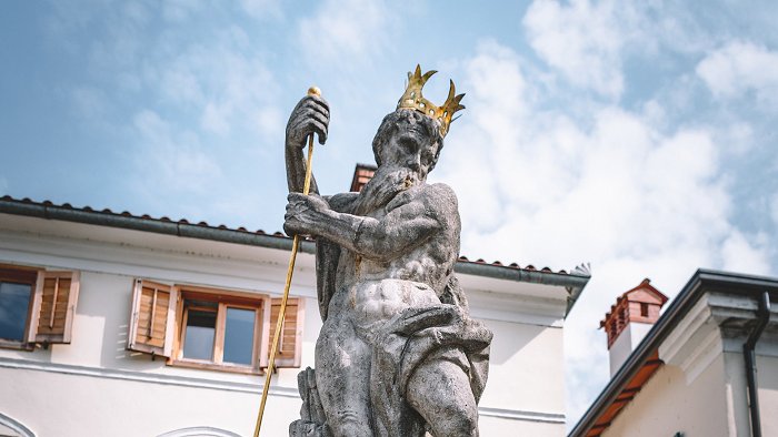 Eine steinerne Neptunstatue mit einer vergoldeten Krone auf dem Kopf und einem vergoldeten Dreizack in der Hand