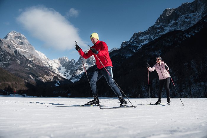 Cross-country skiers enjoy the groomed piste with Mount Mangart and the Loška stena wall in the background.