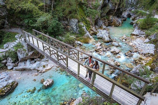 La famiglia gode della vista dal ponte di legno che attraversa il fiume Tolminka verde-azzurro.