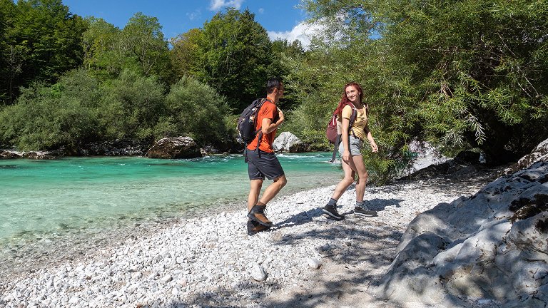 The hikers are walking along the sandy bank of the Soča River